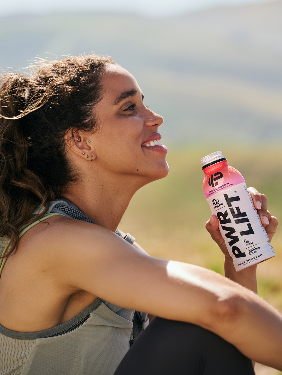A woman resting after a workout with a bottle of PWR Lift Berry Strawberry